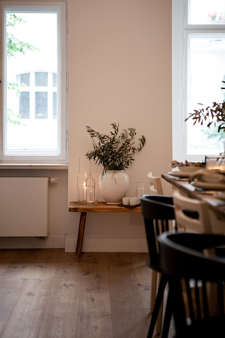 Vase with twigs on wooden bench, candles next to it, dining room