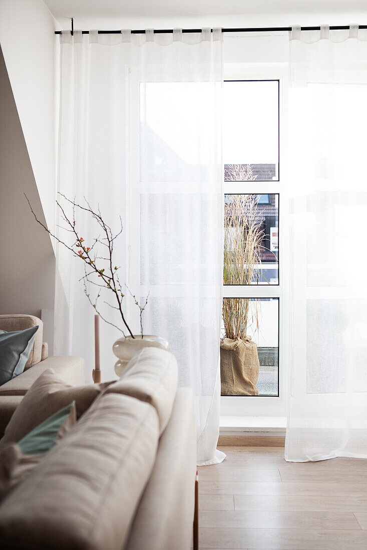 Helles Wohnzimmer mit transparenten Vorhängen und Blick auf Balkon