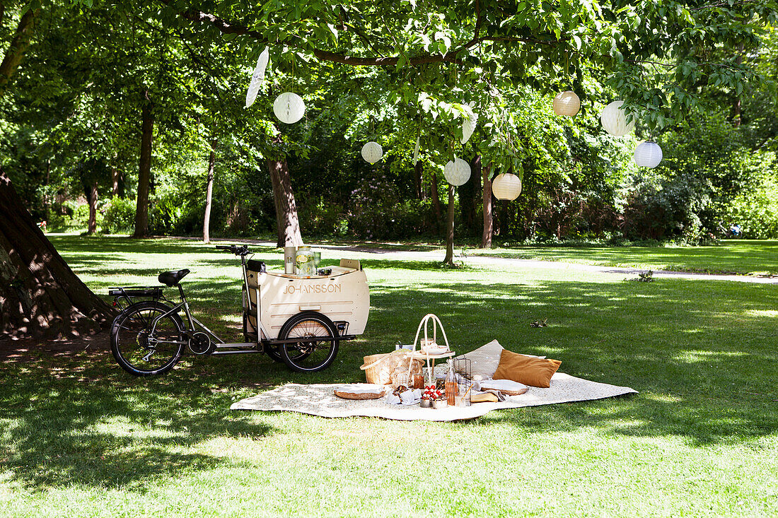 Picknick unter einem Baum mit Fahrradbollerwagen und Laternen im Park