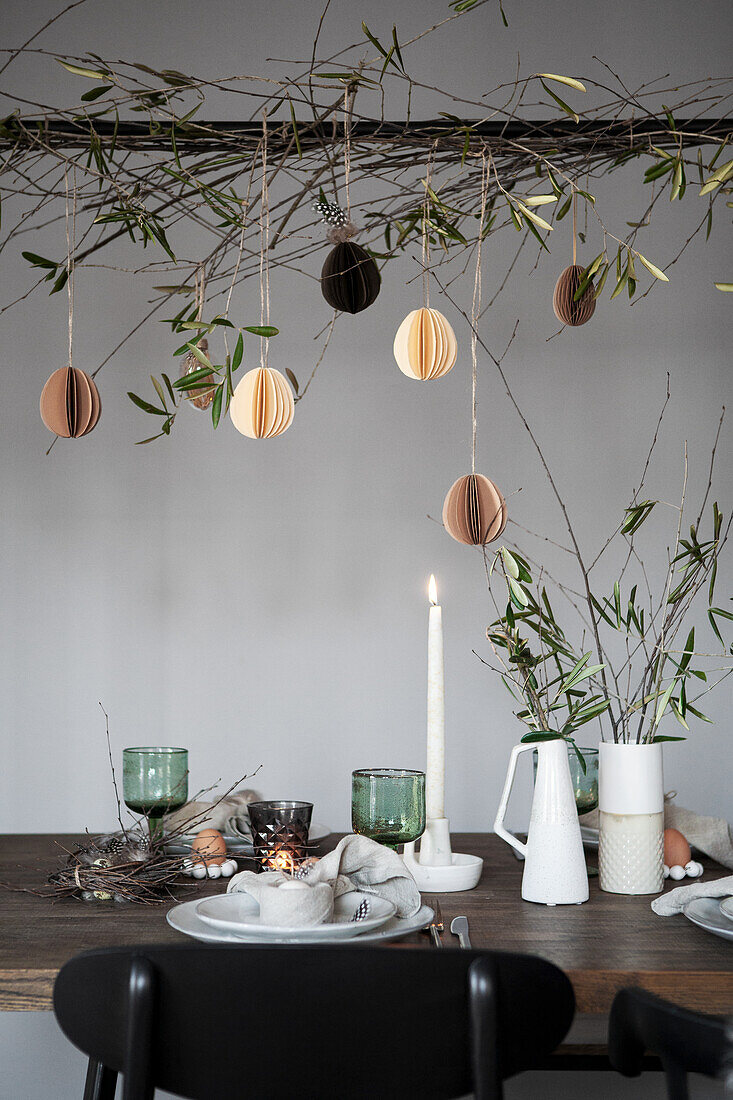 Easter decoration with hanging paper eggs and olive branches above a laid table