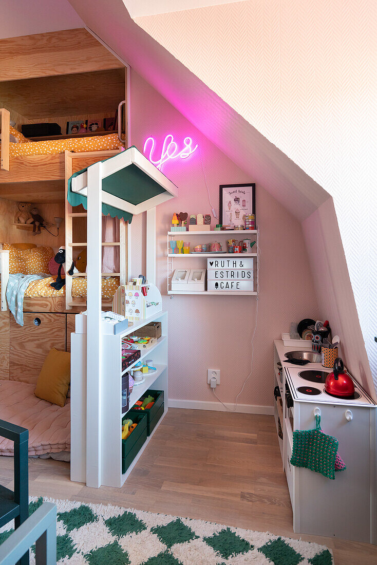 Children's room with sloping roof, play kitchen, shop, shelf, illuminated lettering and bunk bed