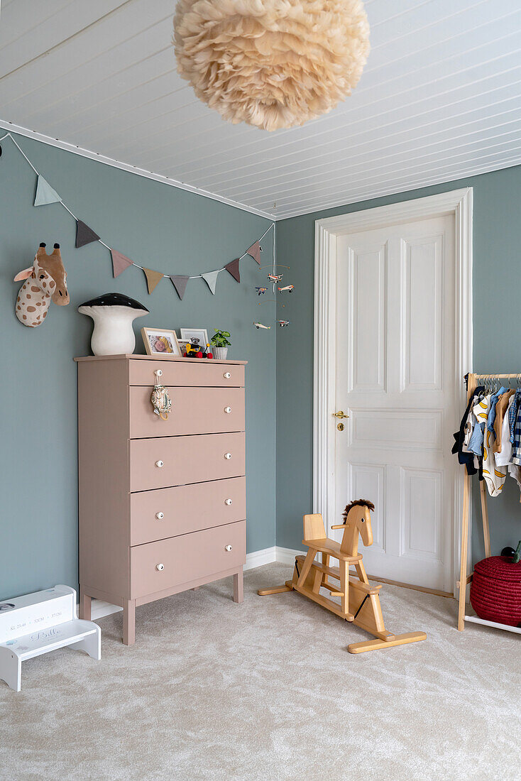 Kinderzimmer mit Wimpelkette, Kommode in Pastellrosa, Schaukelpferd und Wänden in Blau