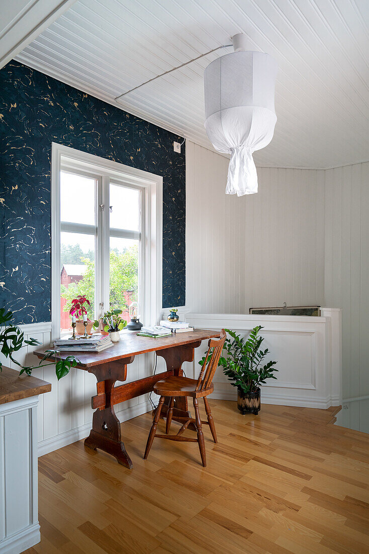 Wooden desk in front of window and dark patterned wallpaper