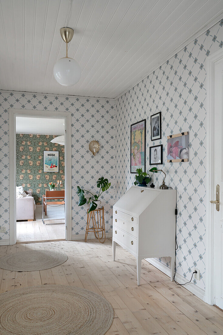 Hallway with white chest of drawers, picture gallery and round rugs on wooden floor