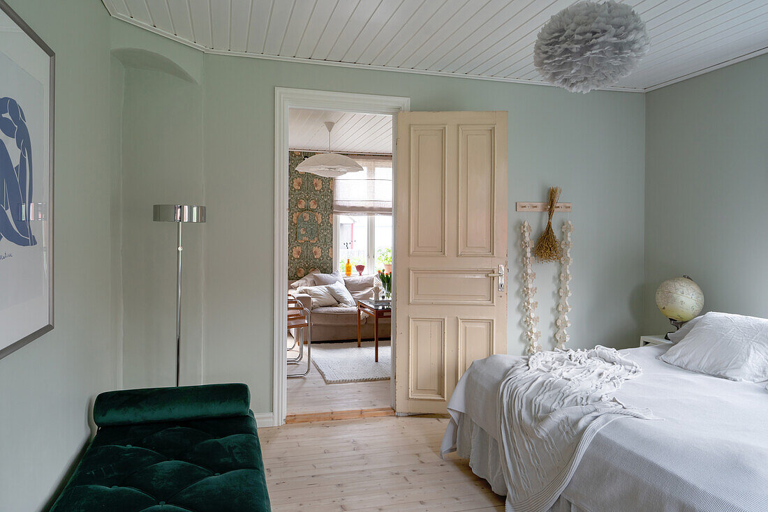 Grünes Daybed und weißes Bett in einem Schlafzimmer mit Blick ins Wohnzimmer