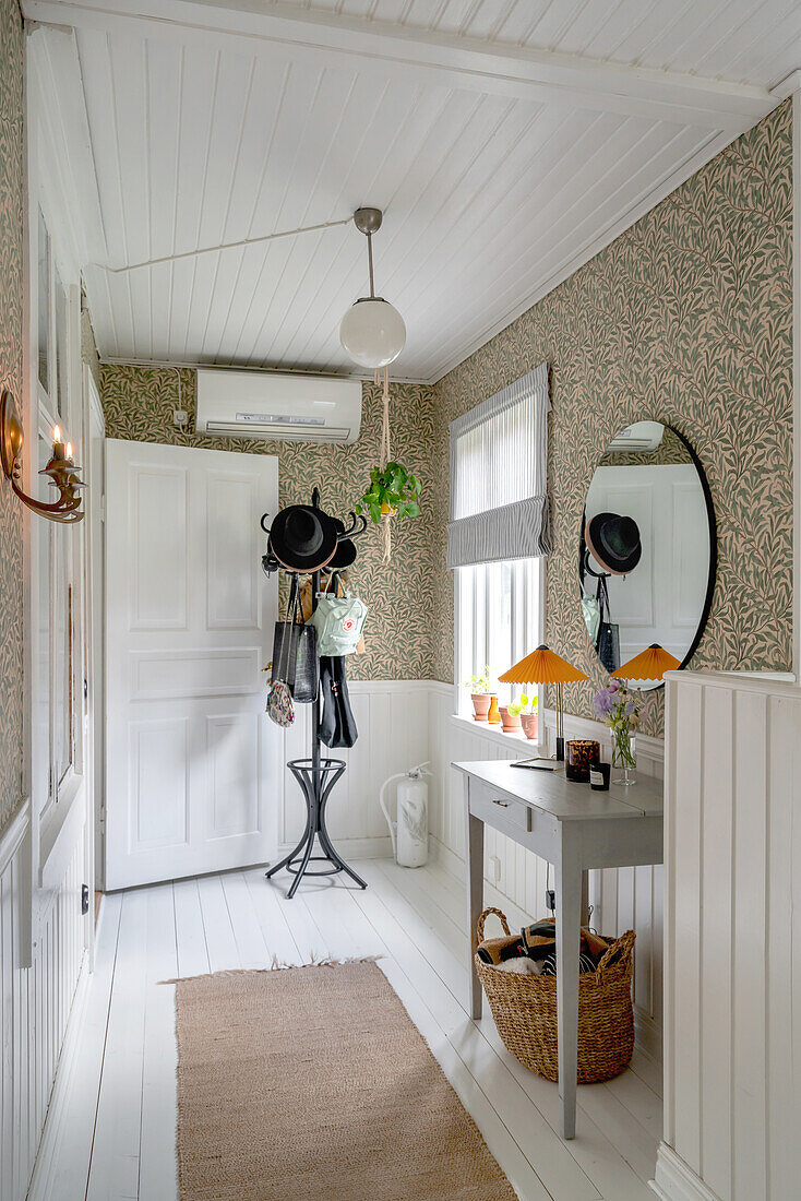 Hallway with patterned wallpaper and white floorboards, coat rack and console table