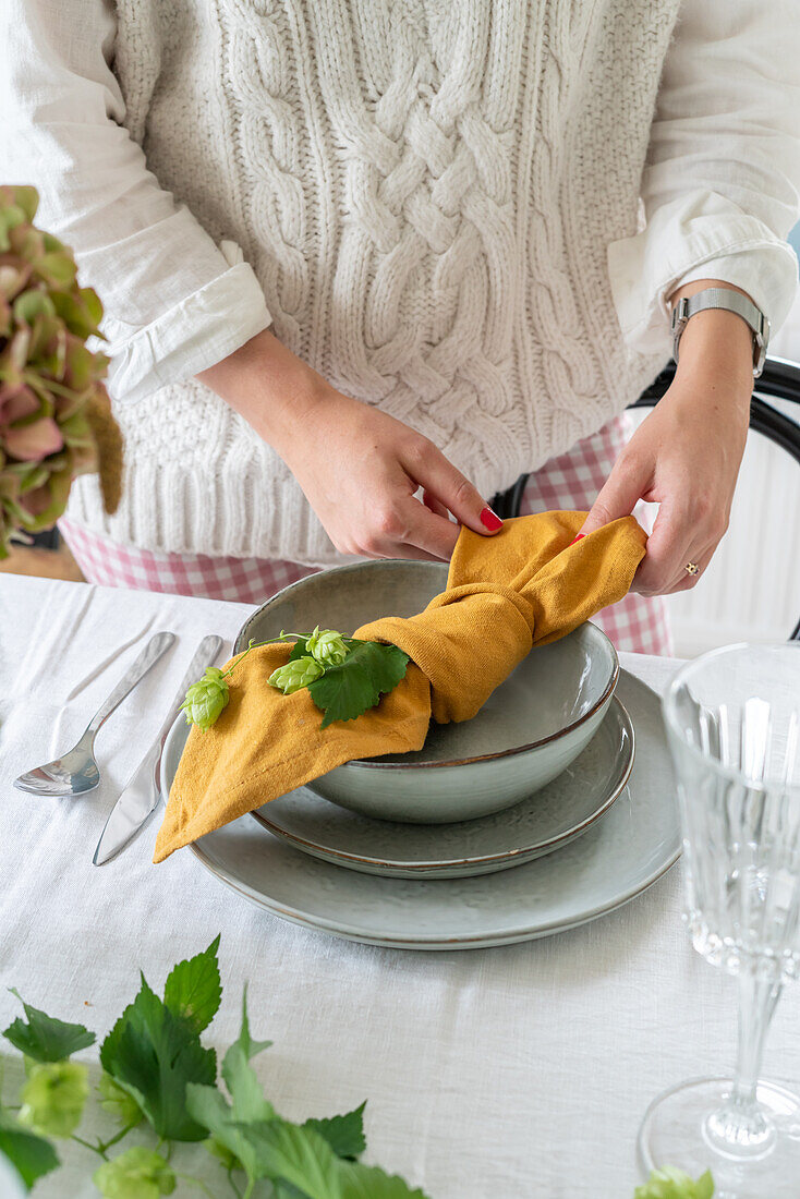 Woman decorates dining table with cloth napkin and hops