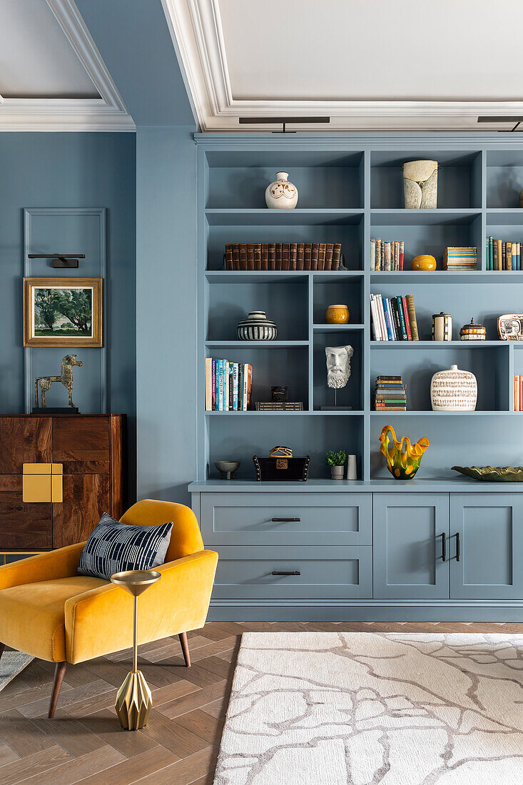 Blaue Regalwand, elegantes Highboard und gelber Sessel im Wohnzimmer