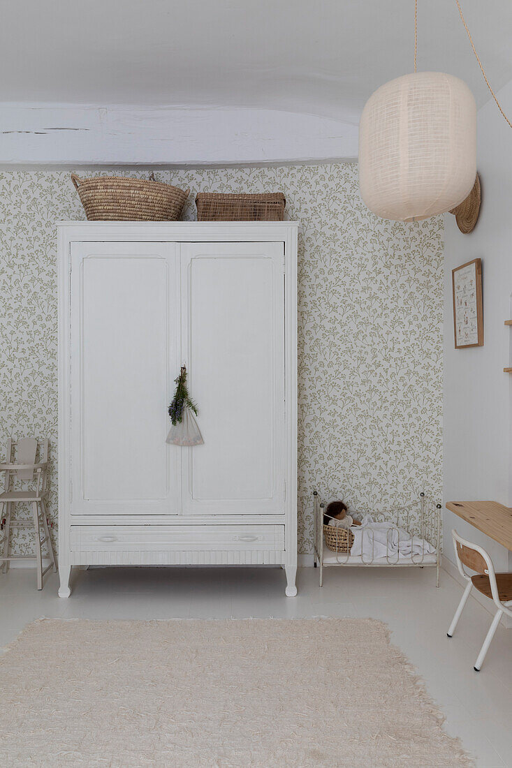 White vintage cupboard in front of patterned wallpaper in a bright children's room