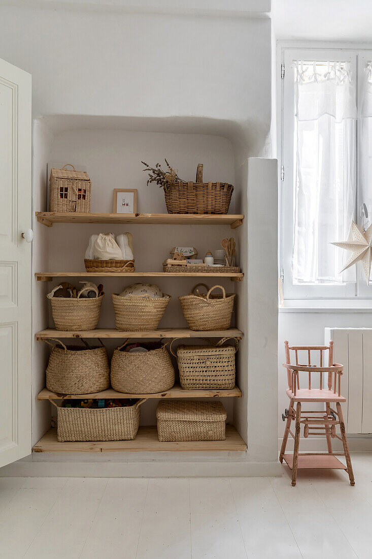 Shelf with baskets in different sizes and wooden children's chair in a bright room