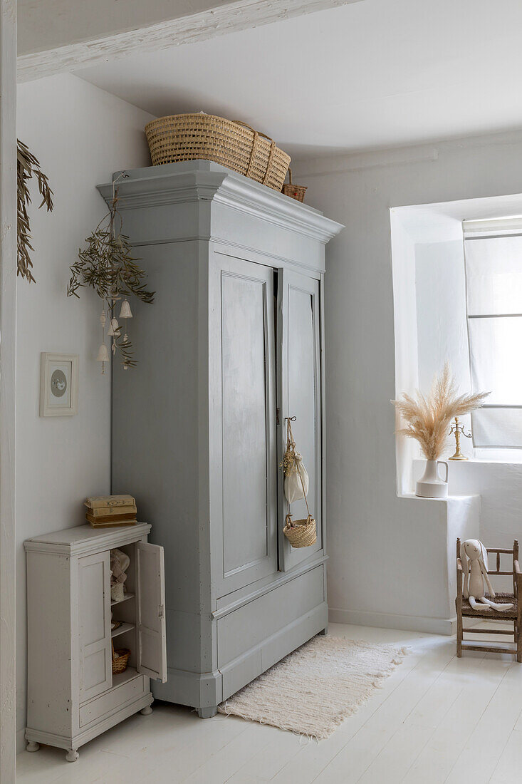 Grey wardrobe in light-coloured children's room with white-painted wooden floor