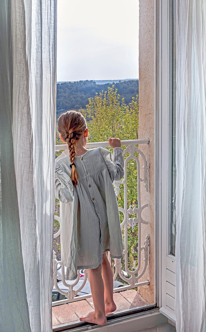 Girl in a casual dress standing on a balcony with a view of the countryside