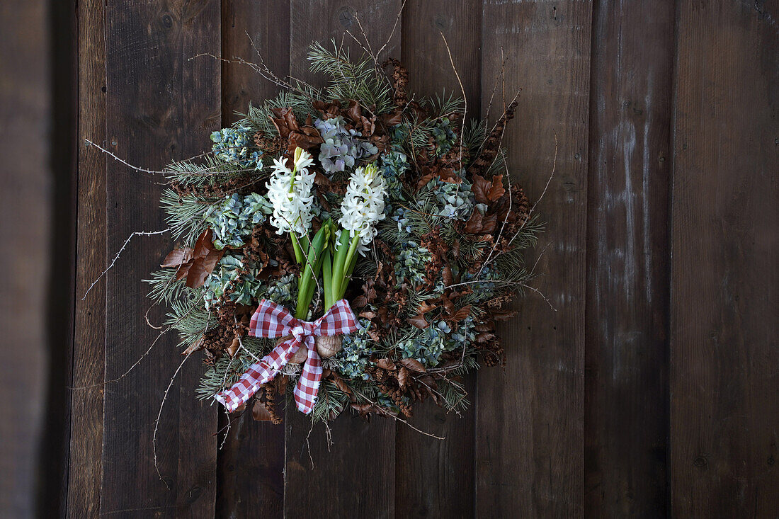 Winterkranz aus Naturmaterialien wie Lärchenzweige, Kiefernzweige, getrockneten Hortensien, Rotbuchenblätter und Farnzweige, weiße Hyazinthen (Hyacinthus) mit Knolle