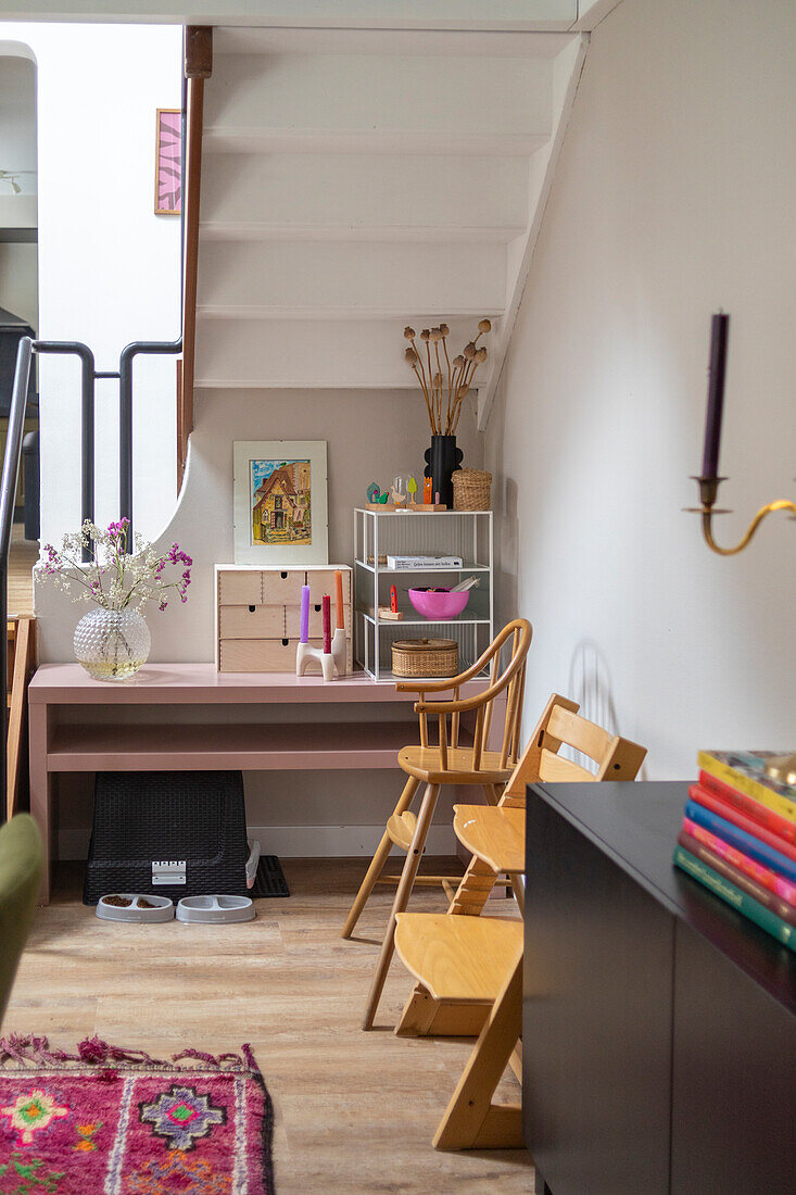 Pink table under a white staircase, wooden high chairs for children