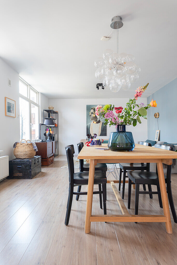 Bright dining room with wooden table, bouquet of flowers and modern lamp