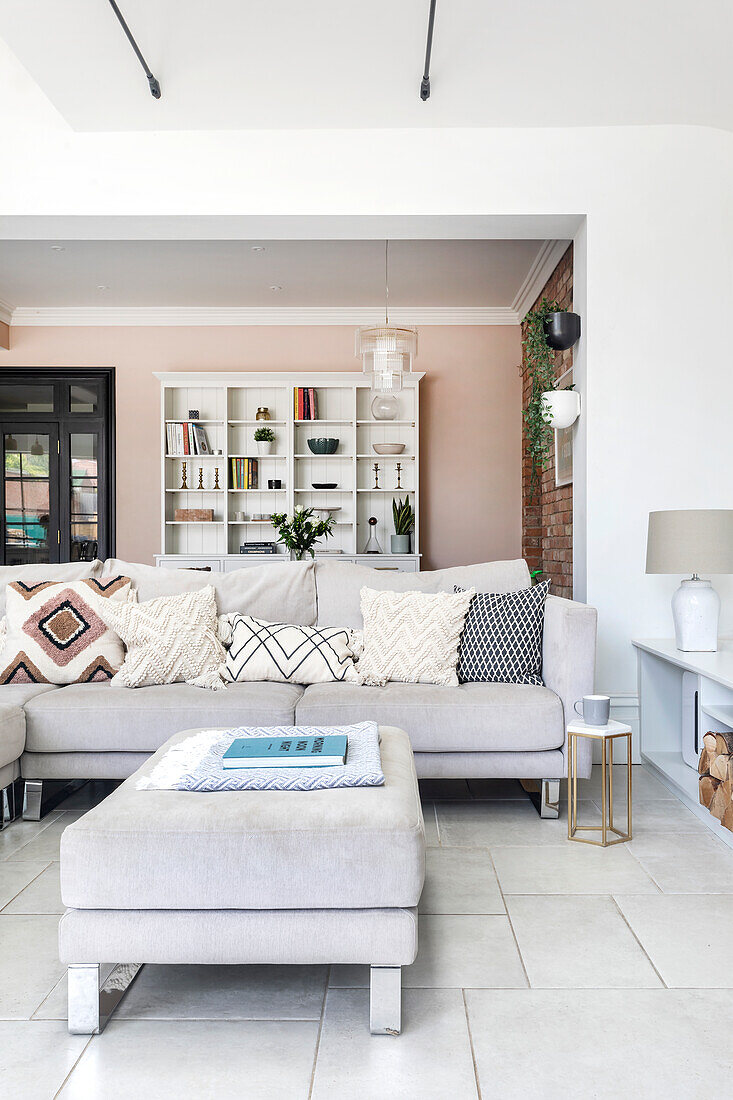 Bright living room with large corner sofa, patterned cushions and bookshelf in the background