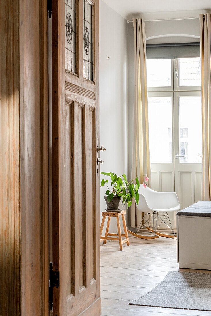 View through wooden door to bright room with green plant and modern chair