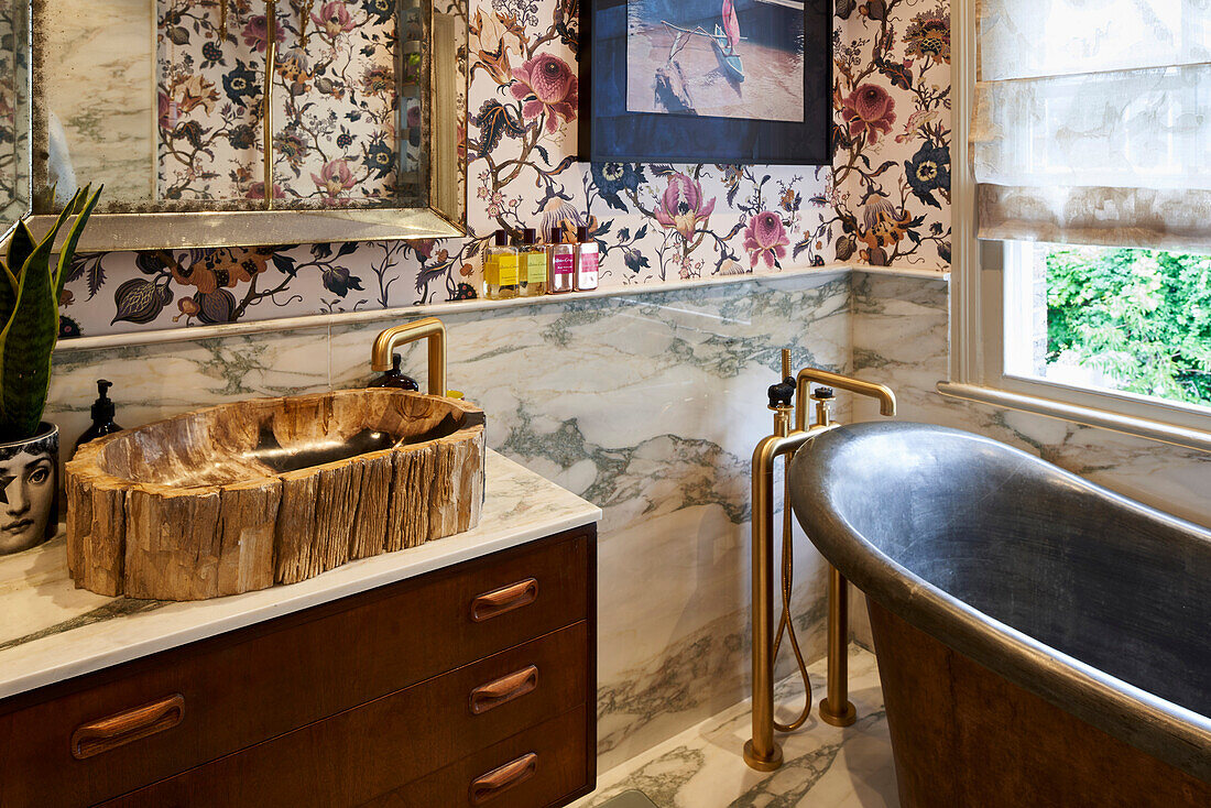 Natural stone sink and vintage bathtub in a bathroom with marble tiles and wallpaper