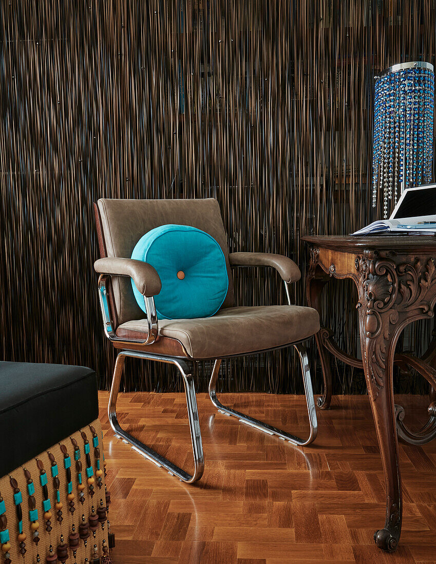 Retro-Bürostuhl mit türkisfarbenem Kissen vor verziertem Holzschreibtisch
