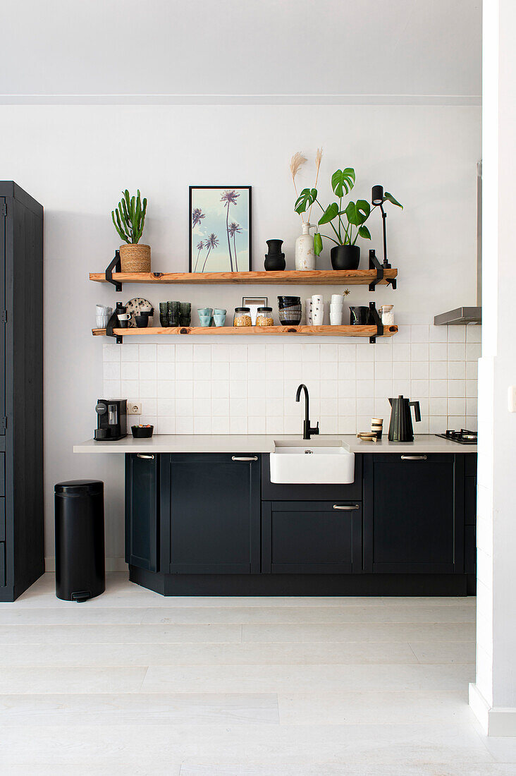 Black kitchen unit with light-colored worktop, wooden shelves above