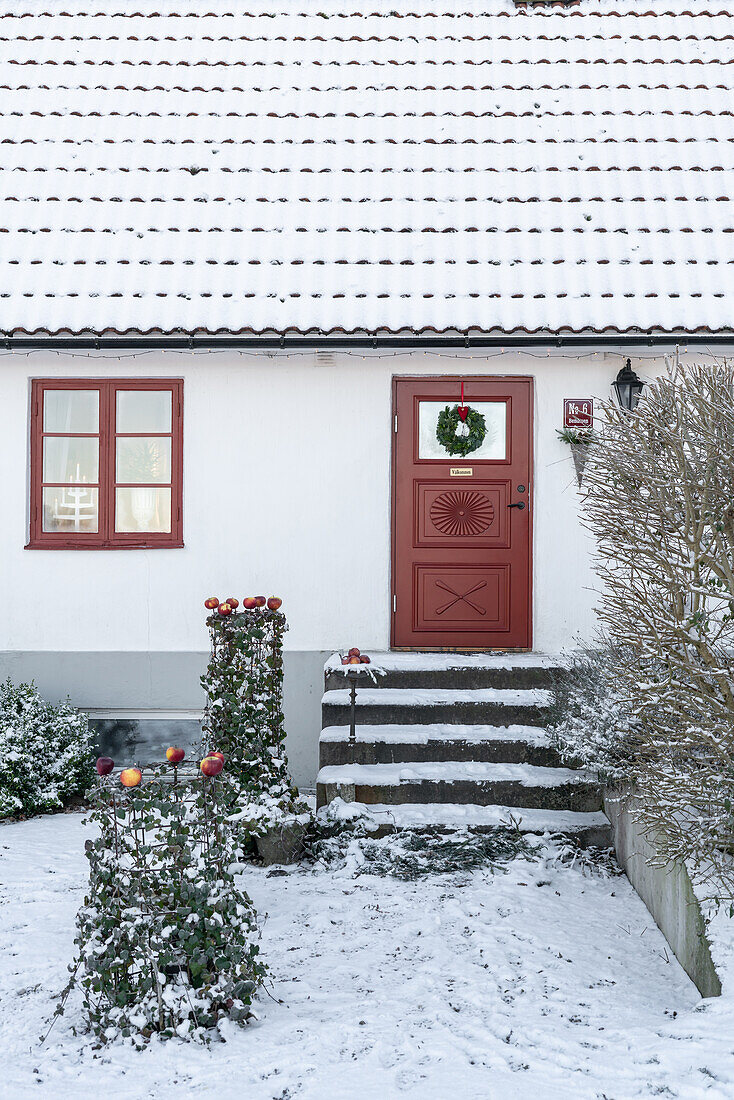 Hauseingang mit roter Tür und Weihnachtsdekoration im Schnee