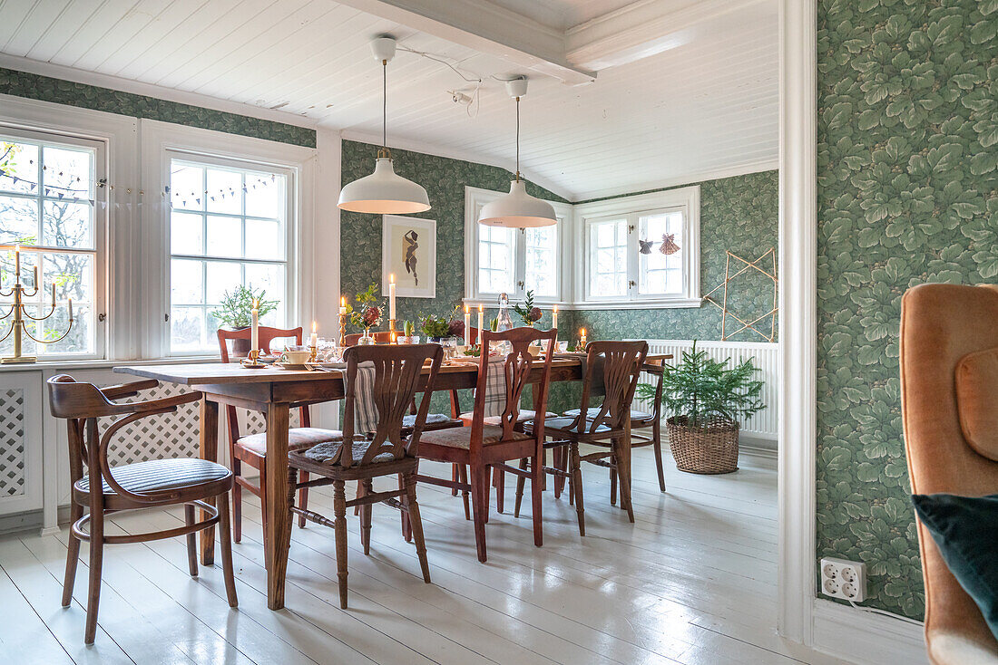 Dining room with wooden table, upholstered chairs and wallpaper with leaf motif