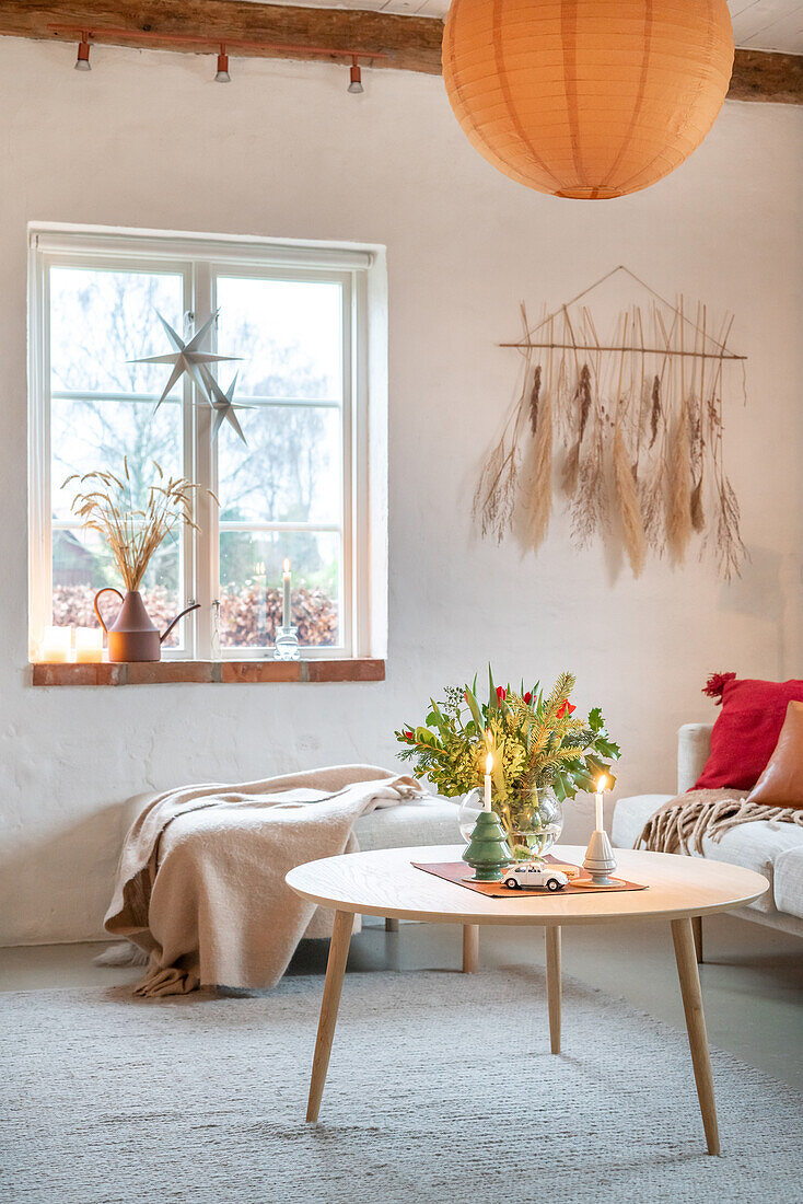 Hell gestalteter Wohnraum mit rundem Holz-Couchtisch und Trockenblumen an der Wand