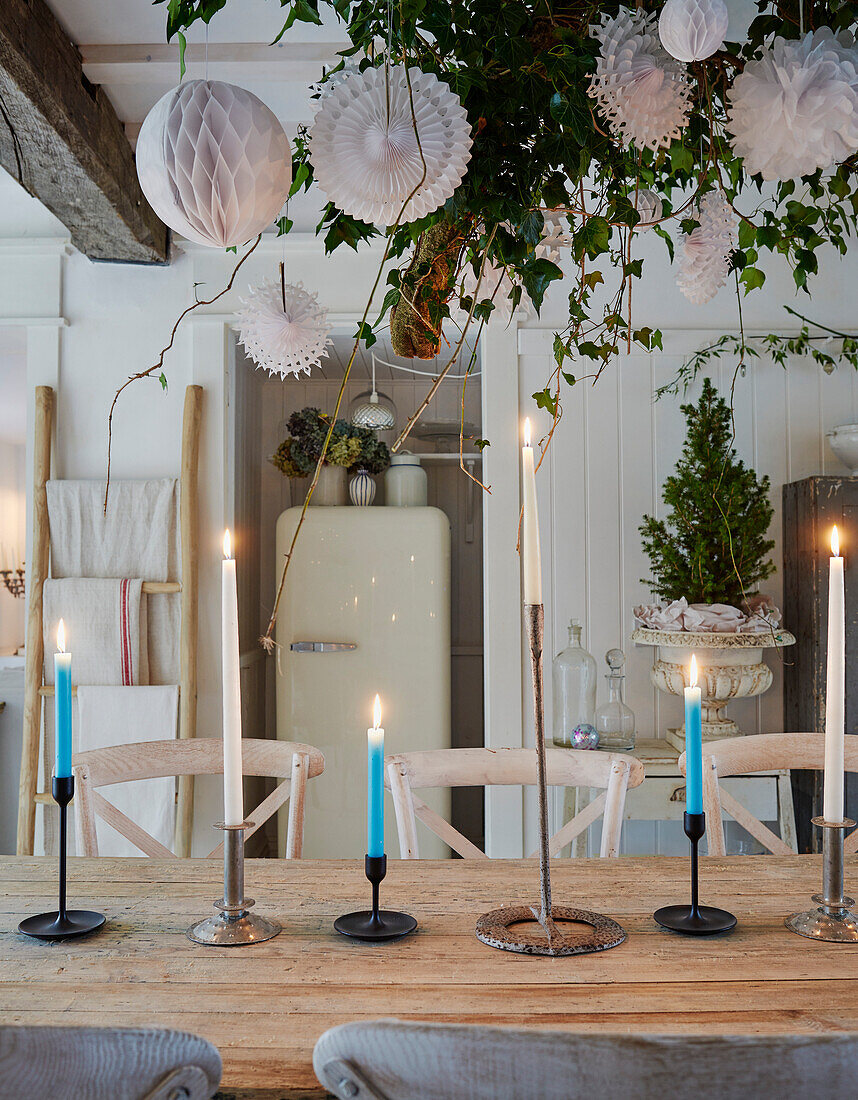 Wooden table with blue candles and hanging paper decorations in dining room