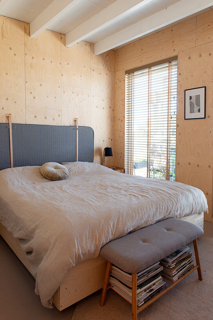 Double bed and bench in the bedroom with light-colored wood paneling