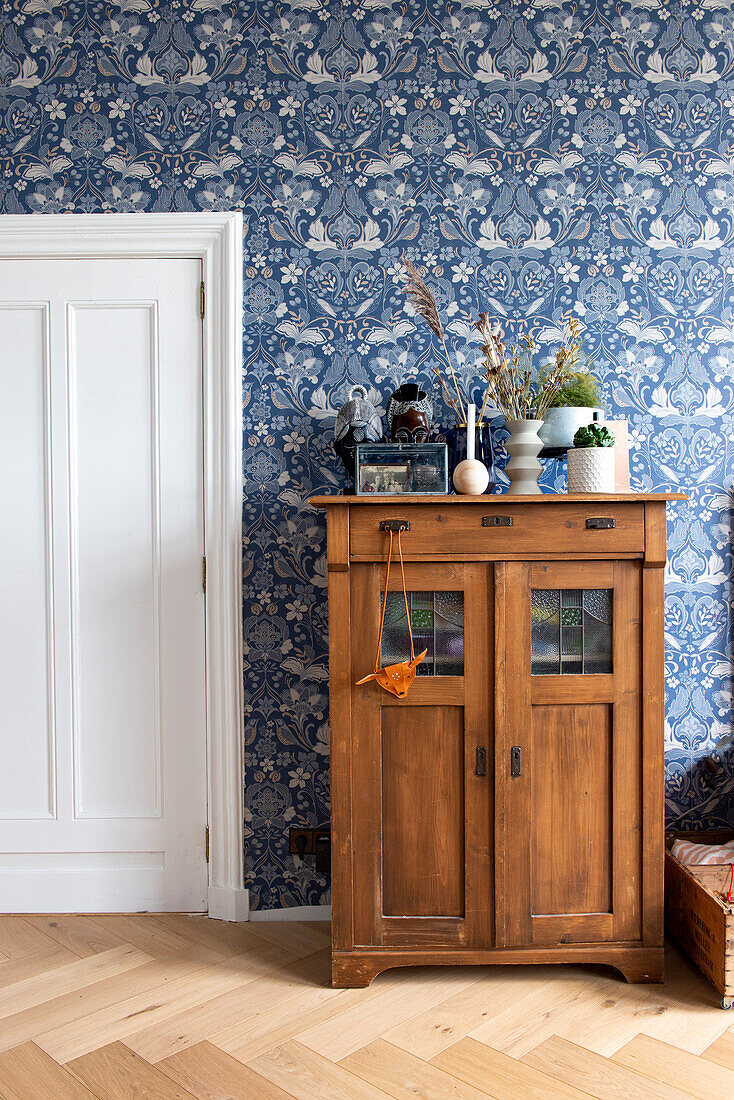 Antique wooden cupboard in front of blue and white patterned wallpaper
