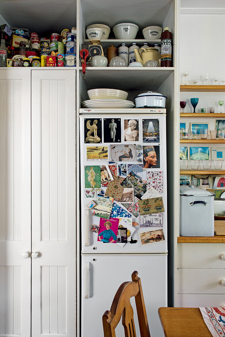 White cupboard with storage containers and bowls and fridge with colorful postcards