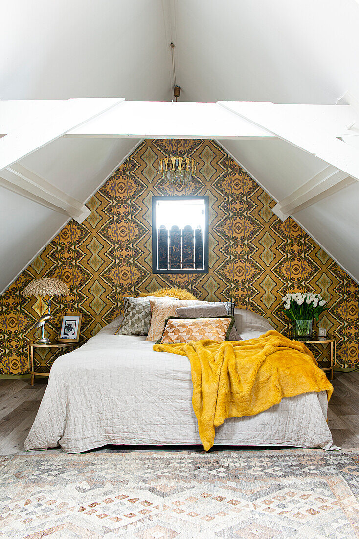 Bedroom with patterned wallpaper, sloping ceilings and yellow blanket on bed