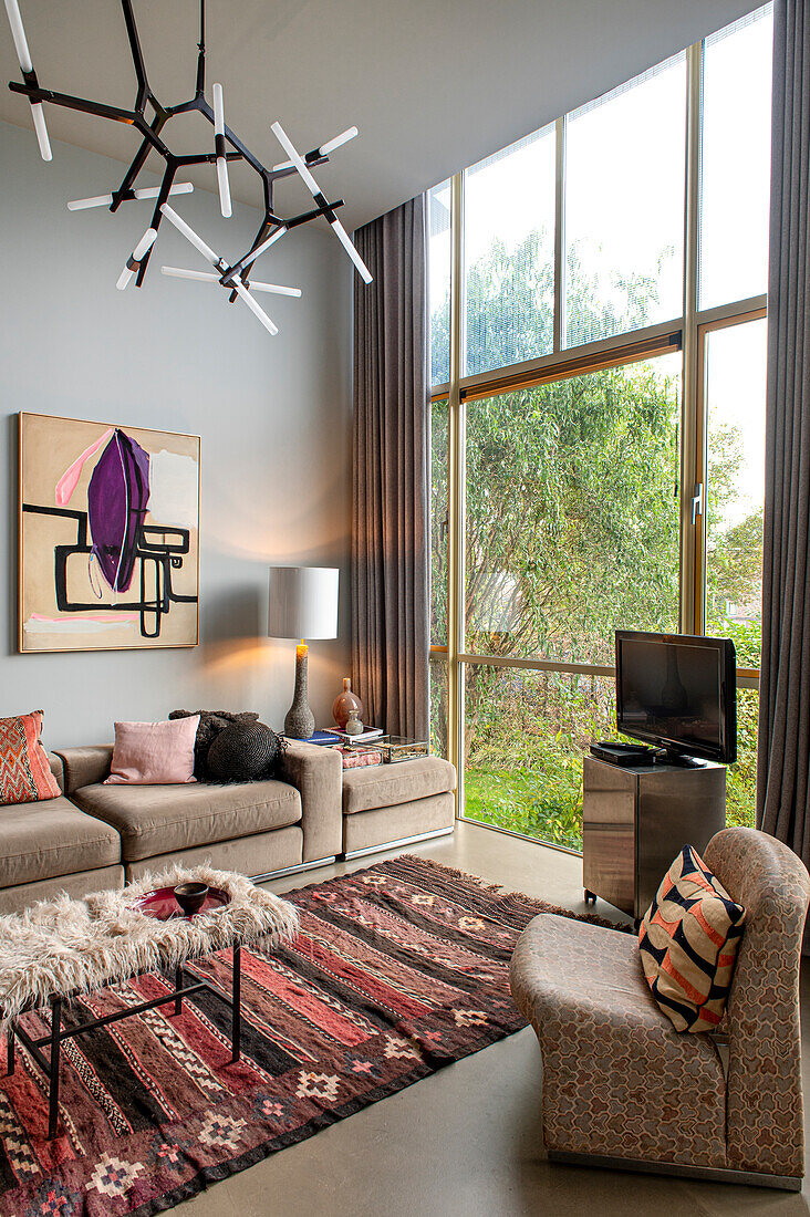 Upholstered sofa, colourful carpet and designer lamp in the living room with floor-to-ceiling glazing