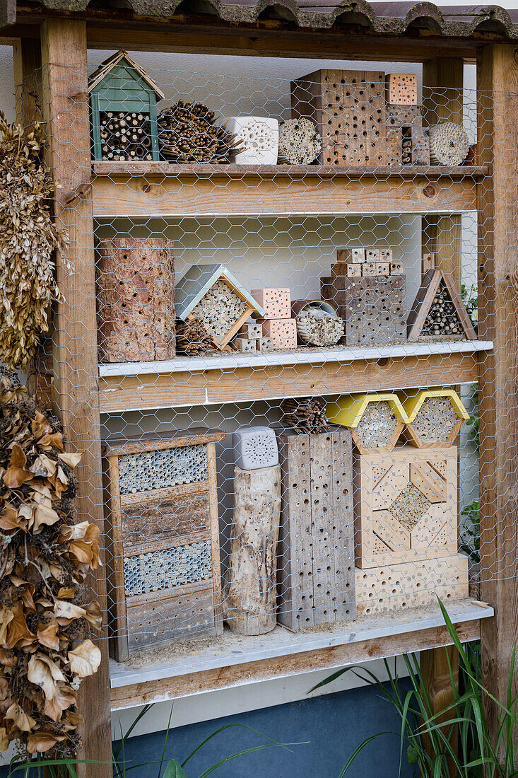 Holzregal mit verschiedenen Insektenhotels im Garten