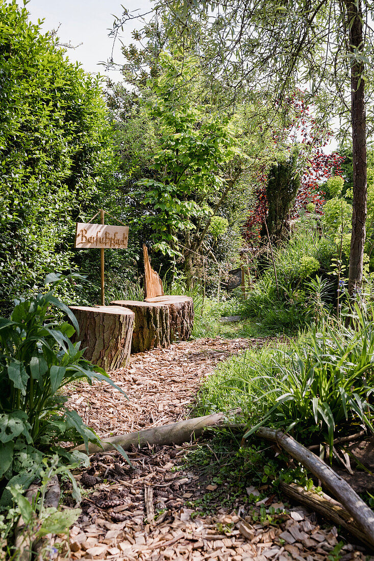 Natural garden path with wood chips, sign and tree trunk seat