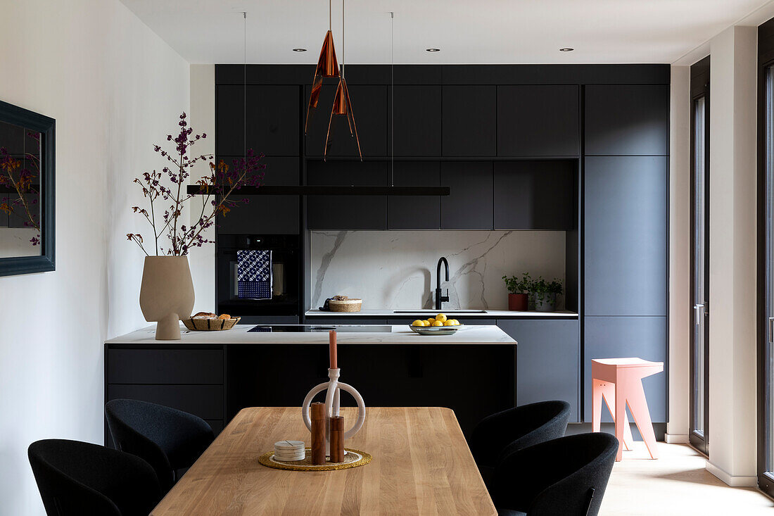 Modern kitchen in black and white with wooden dining table and copper lamps