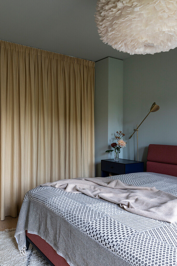 Bedroom with cream-coloured curtains, feather lamp and burgundy headboard