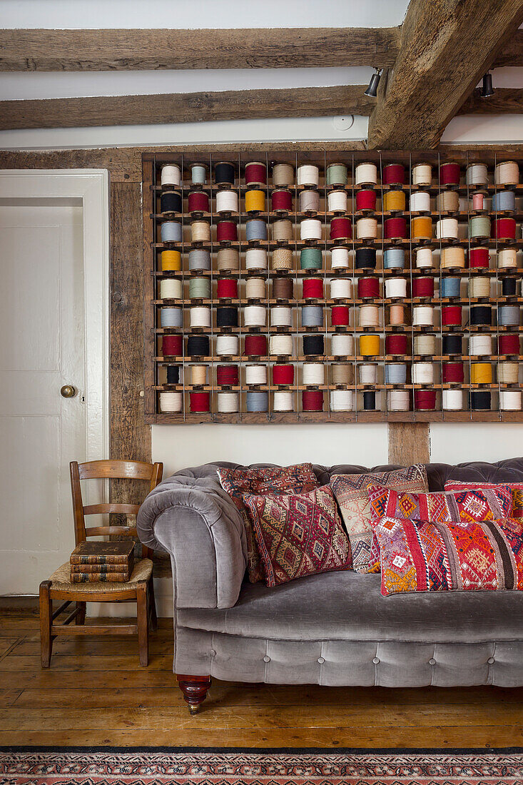 Grey velvet sofa with colourful cushions in front of shelf with colourful spools of yarn