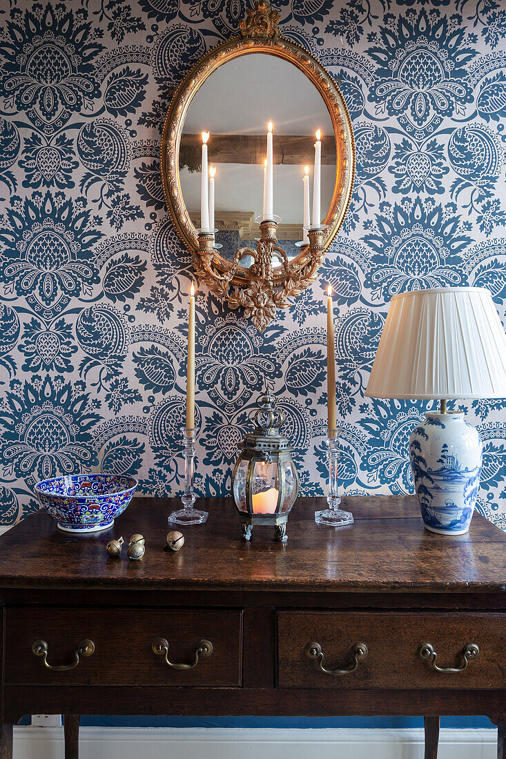 Antique wooden table with candles and lamp in front of blue and white wallpaper