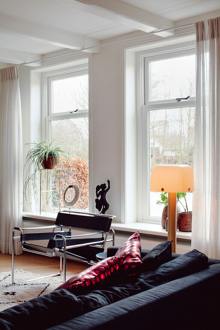 Helles Wohnzimmer mit großer Fensterfront und schwarzen Sitzmöbeln