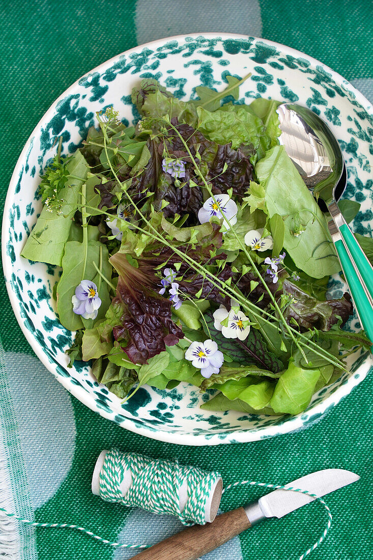 Bowl with mixed leaf salad and edible flowers on green tablecloth