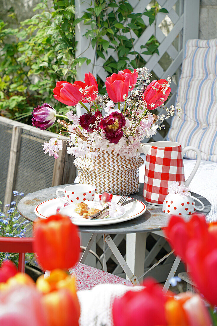 Bunter Frühlingsstrauß auf Gartentisch mit Kaffee und Kuchen