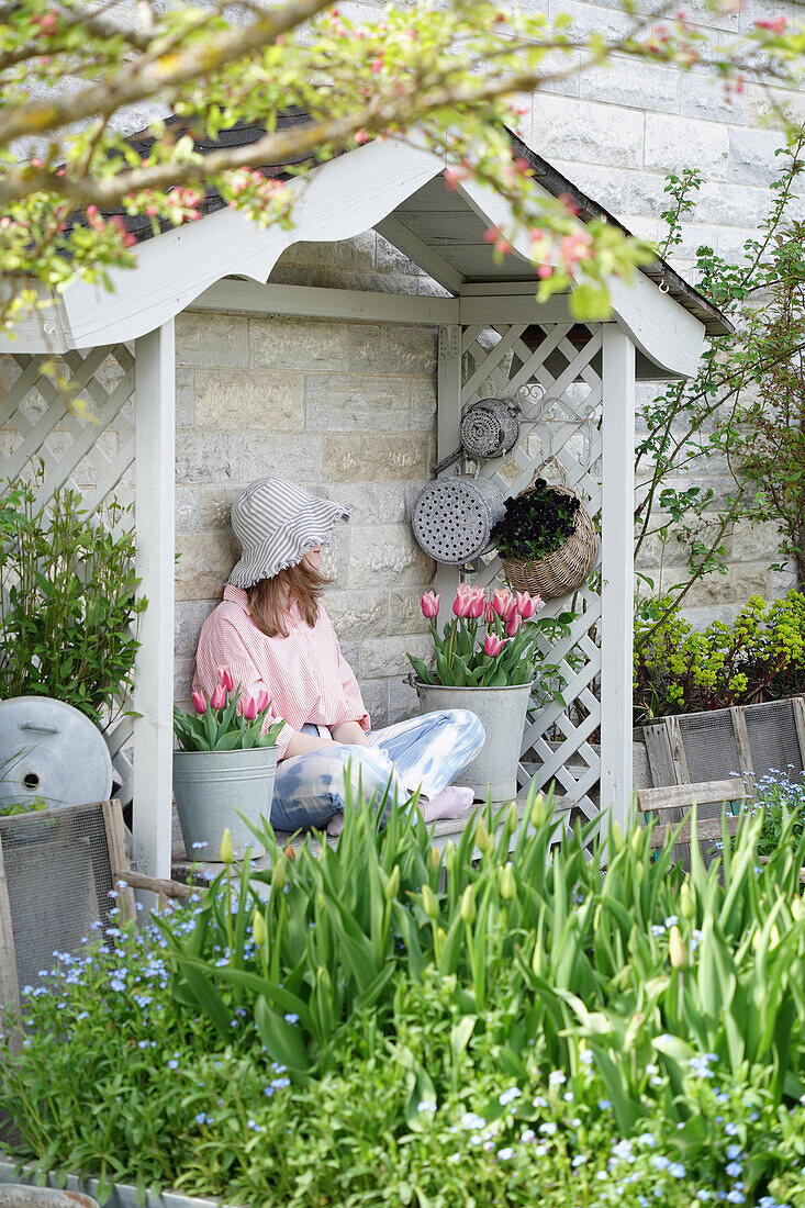 Person entspannt in einer Gartenlaube umgeben von Frühlingsblumen