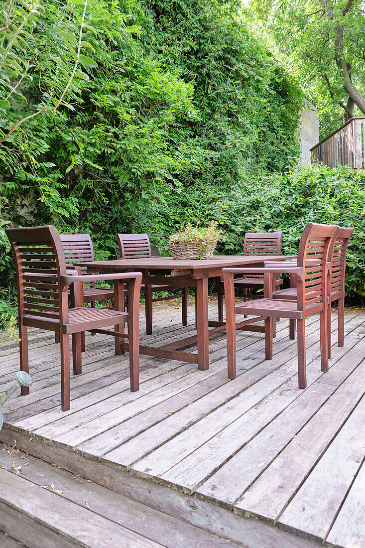 Holztisch und Stühle auf Terrasse mit grüner Hecke im Hintergrund