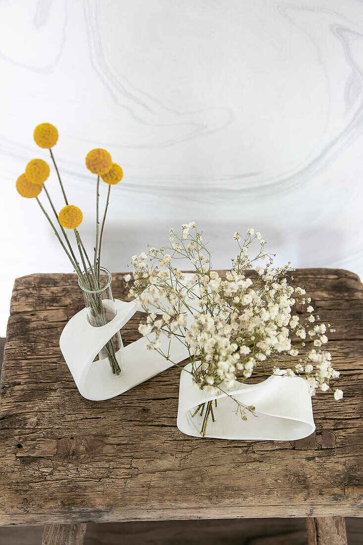 Two modern vases with yellow drumsticks (Craspedia) and baby's breath (gypsophila) on a wooden stool