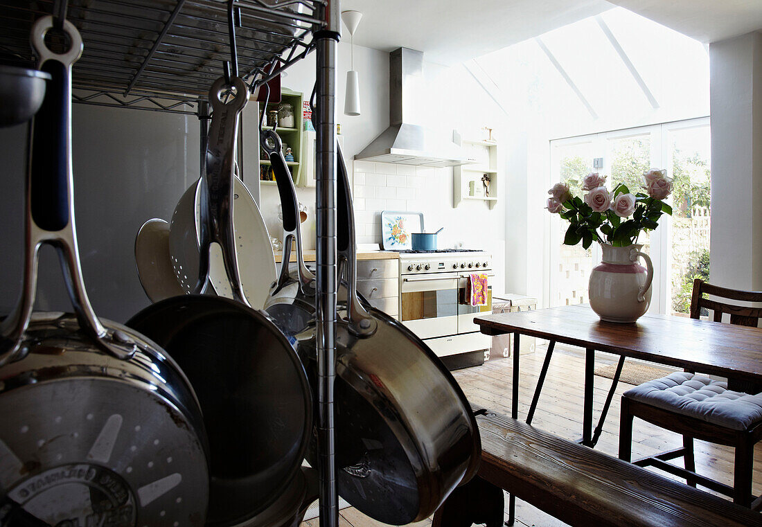 Saucepans hang on rack in open plan kitchen extension with cut roses on wooden table Brighton home East Sussex, England, UK