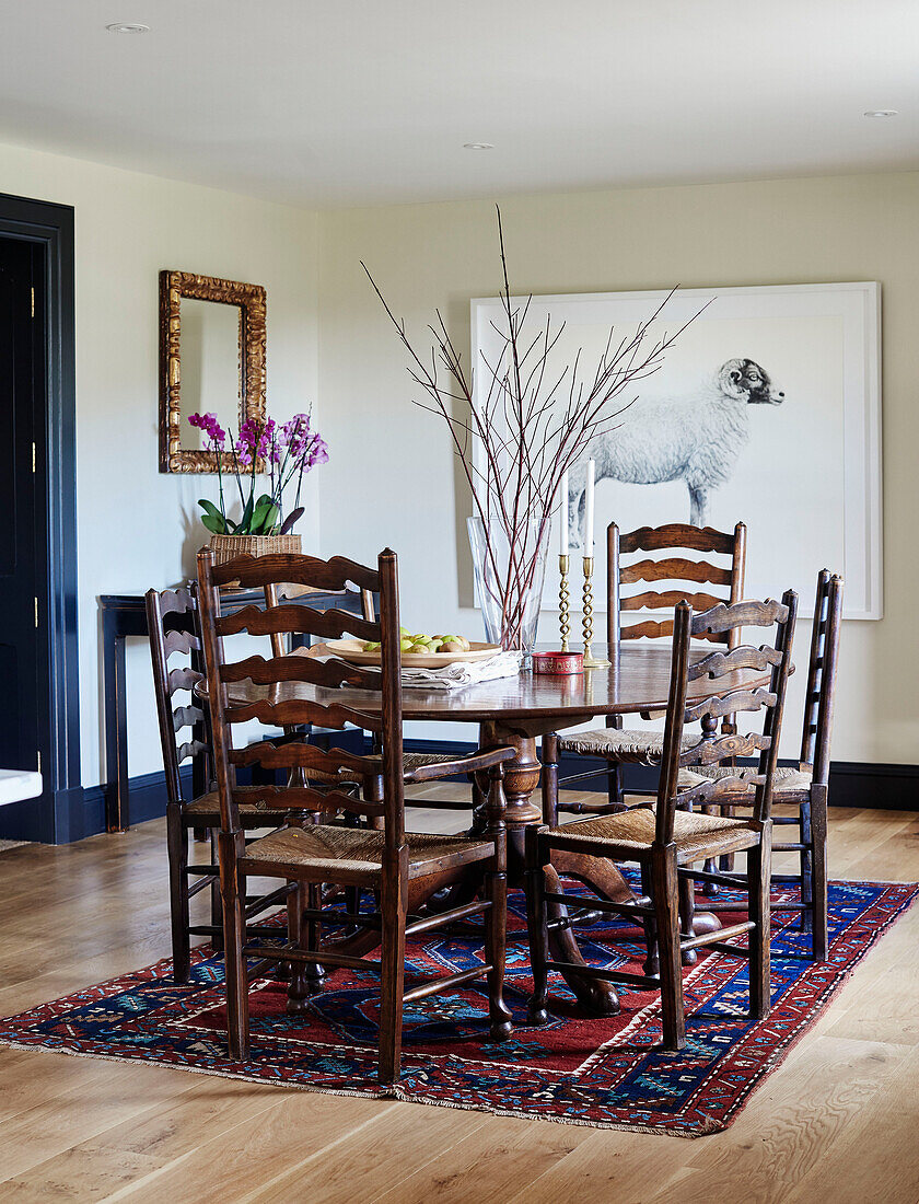 Dining table and chairs with patterned rug and artwork of ram in North Yorkshire farmhouse, UK