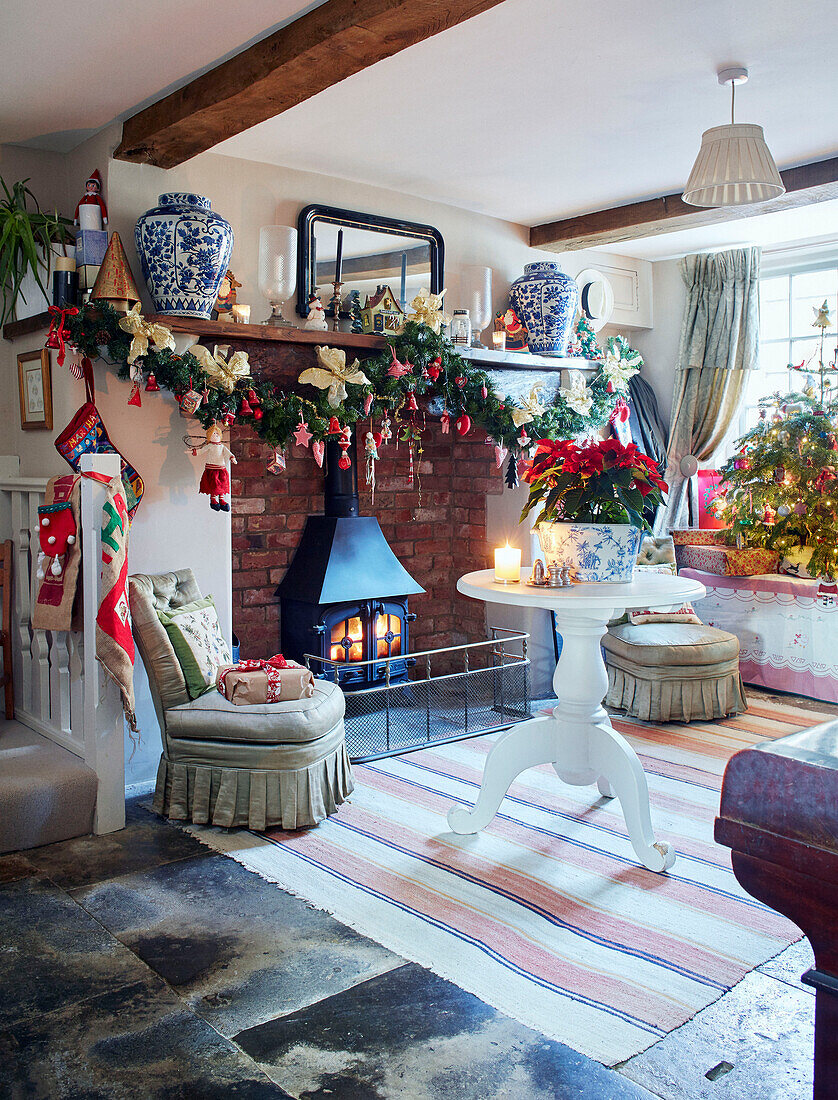 Weihnachtsgirlande über einem beleuchteten Holzofen mit Weihnachtsstern auf einem Sockeltisch in einem britischen Cottage