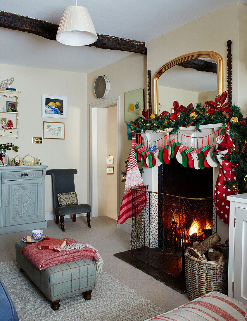 Weihnachtsstrümpfe hängen über Kamin mit Feuer und Spiege, davor Fußhocker in einem britischen Haus