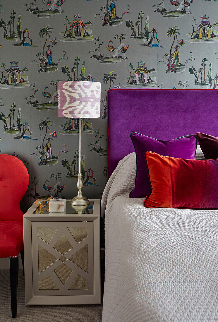 Lila Kopfteil und orientalische Tapete mit roten Samtkissen und Stuhl in Londoner Wohnung, UK